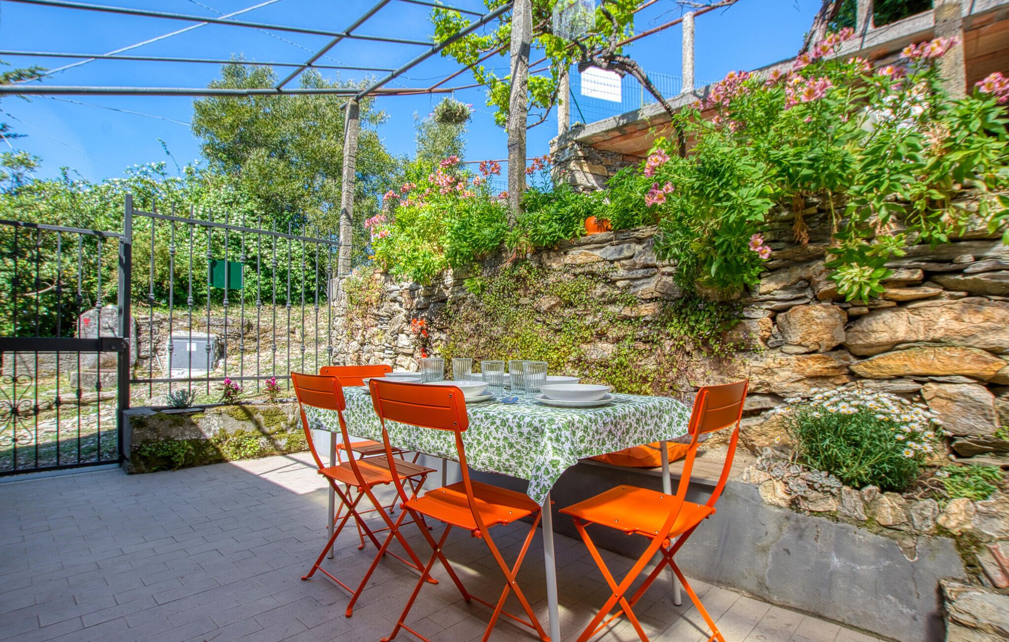 An outdoor patio with a table set for four, surrounded by orange chairs, under a metal pergola.