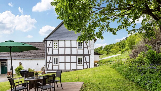 A traditional half-timbered house with a deck, outdoor furniture, and a green umbrella. - Apartment 'Fewo Am Uplandsteig' with Shared Terrace, Garden and Wi-Fi (Diemelsee)