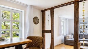 A dining area with a table and chairs, a wooden beam structure, a sofa, and a view through large windows. - Apartment 'Fewo Am Uplandsteig' with Shared Terrace, Garden and Wi-Fi (Diemelsee)