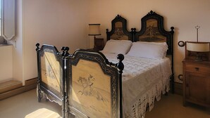 Una cama con dosel decorada con intrincados grabados, una colcha de encaje y una mesita de noche de madera con una lámpara.