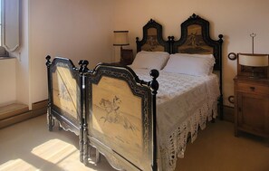 Ein Bett mit Baldachin, verziert mit filigranen Schnitzereien, einem Spitzenüberwurf und einem Nachttisch aus Holz mit Lampe.