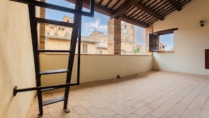 Una habitación con una escalera de madera, piso de baldosas y vistas a edificios históricos a través de una ventana.