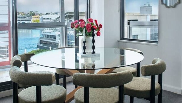 Une salle de conférence moderne avec une table en verre, six chaises et un vase de fleurs.