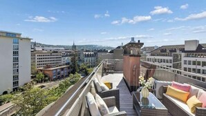 A rooftop terrace with outdoor seating, a view of the cityscape, and a prominent tower structure. - Waterfront Penthouse | AC | Rooftop | Free Parking (Zürich)