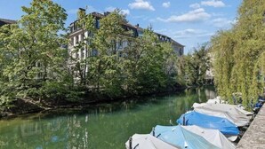 A river with boats docked, trees along the banks, and buildings in the background. - Waterfront Penthouse | AC | Rooftop | Free Parking (Zürich)