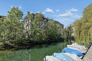 A river with boats docked, trees along the banks, and buildings in the background. - Waterfront Penthouse | AC | Rooftop | Free Parking (Zürich)