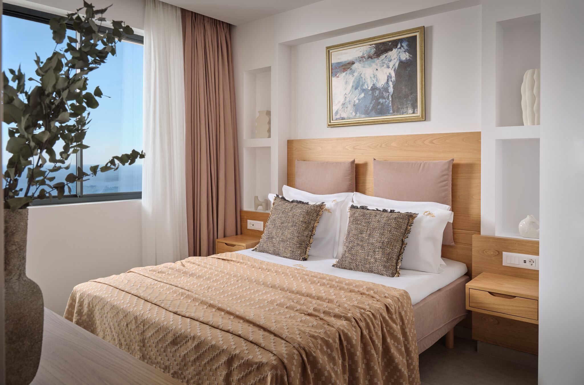 Een keurig opgemaakte slaapkamer met een groot bed, een nachtkastje, een raam met gordijnen, een aan de muur hangend schilderij en een potplant.