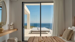 Un dormitorio con una cama grande, vista al océano, una puerta corrediza de vidrio y una pequeña mesa con velas.