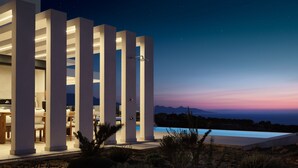Un edificio moderno con piscina, columnas y vistas del paisaje.