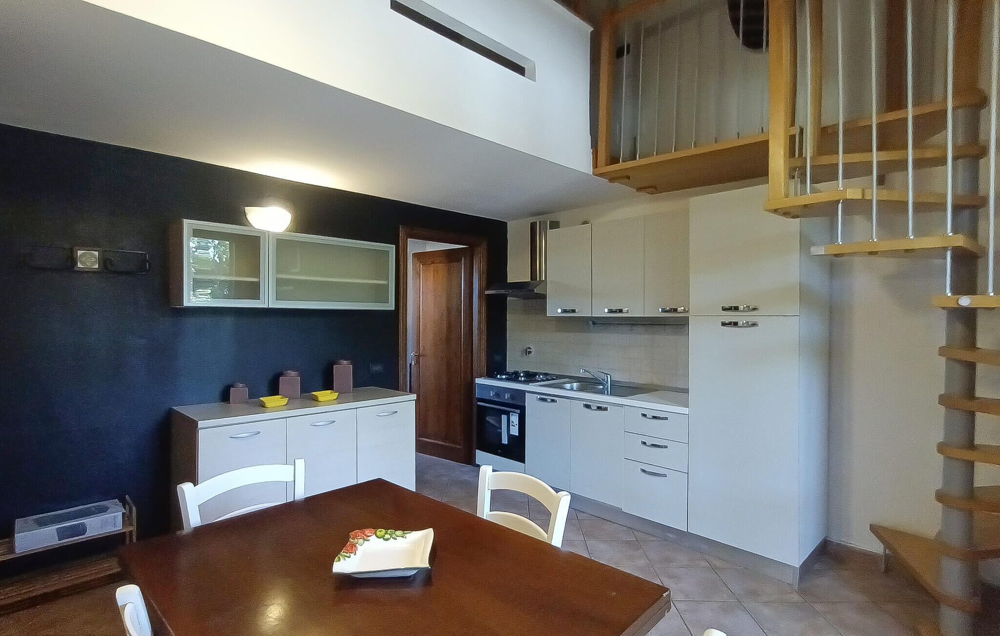 Een kleine keuken met witte kastjes, een kookplaat en een eettafel met stoelen.