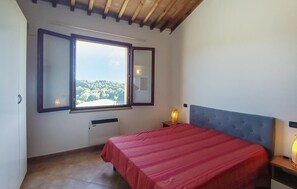 Ein Schlafzimmer mit Bett, einem Fenster mit Blick, einem Heizkörper und einem Nachttisch mit Lampe.