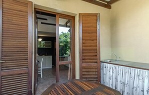 Ein Zimmer mit Holztisch, einer Küchenzeile mit Spüle und einer Schiebetür zu einem weiteren Raum.