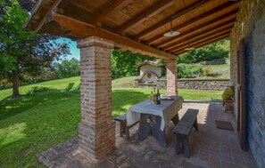 An outdoor patio with a brick table and benches, a stone wall, and a small brick oven in the background. - 2 bedroom awesome home in Pietralunga (Pietralunga)