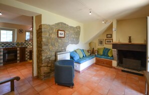 A living room with a stone wall, a sofa, a fireplace, and a kitchen area. - 2 bedroom awesome home in Pietralunga (Pietralunga)