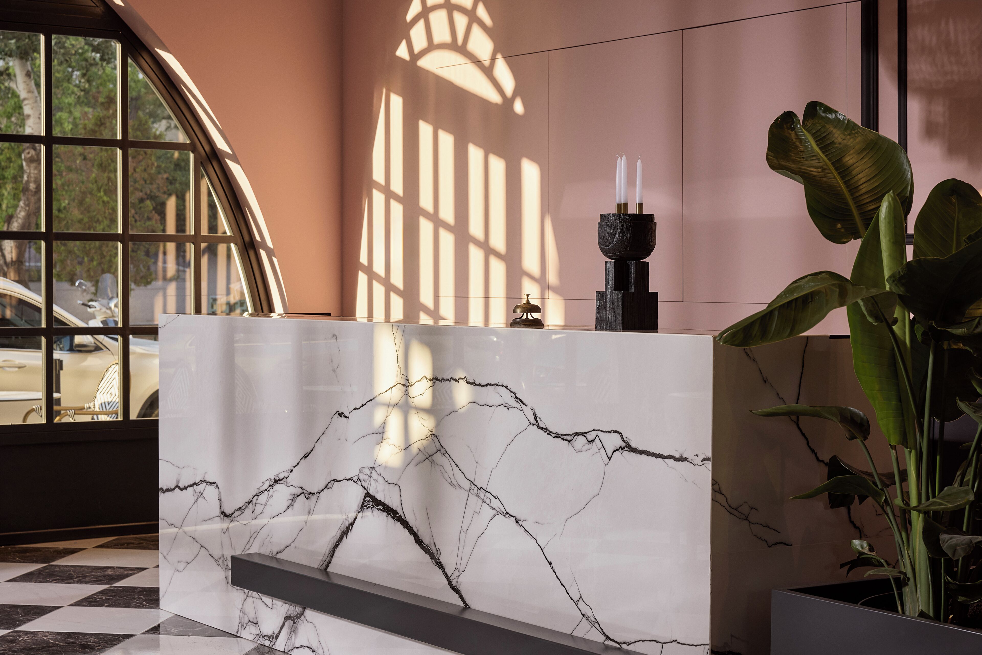 Un comptoir d’accueil au motif de marbre, une plante en pot et une fenêtre laissant entrer la lumière du soleil, qui projette des ombres.