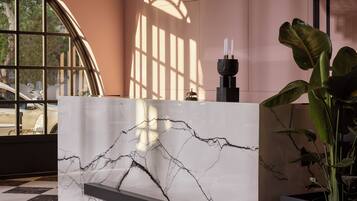 Un comptoir d’accueil au motif de marbre, une plante en pot et une fenêtre laissant entrer la lumière du soleil, qui projette des ombres.