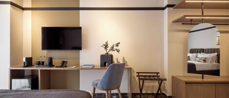 A hotel room with a bed, a desk with a chair, a television, a mirror, and a small table with a vase.