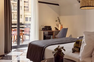 Habitación de hotel con cama, escritorio con silla, planta en maceta y vistas al balcón exterior.