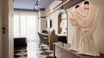 Habitación de hotel con piso a cuadros, un escritorio con una silla, una cama, un espejo y dos batas de baño blancas colgadas en un perchero.