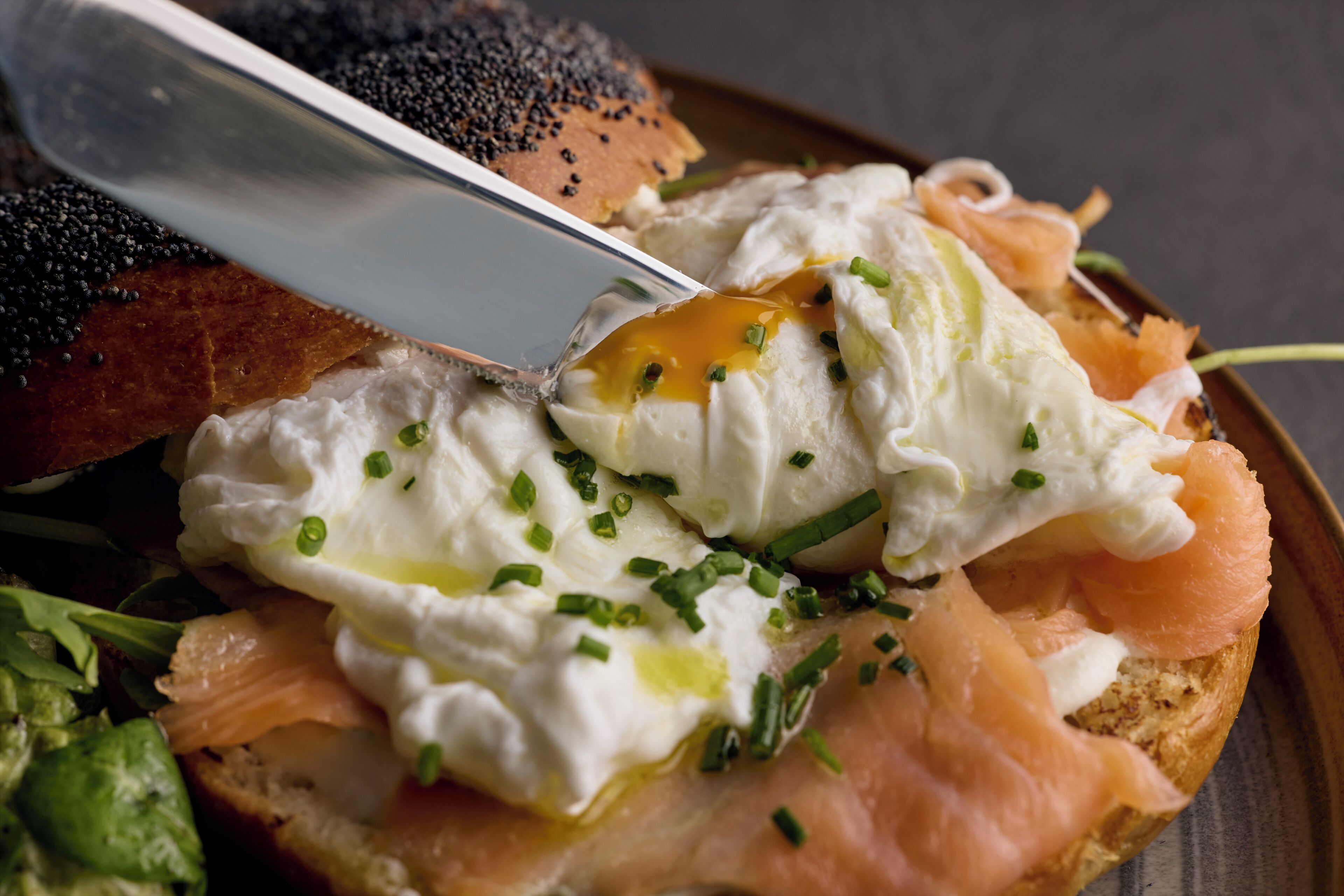 A breakfast plate with eggs, smoked salmon, and chives on a slice of bread.