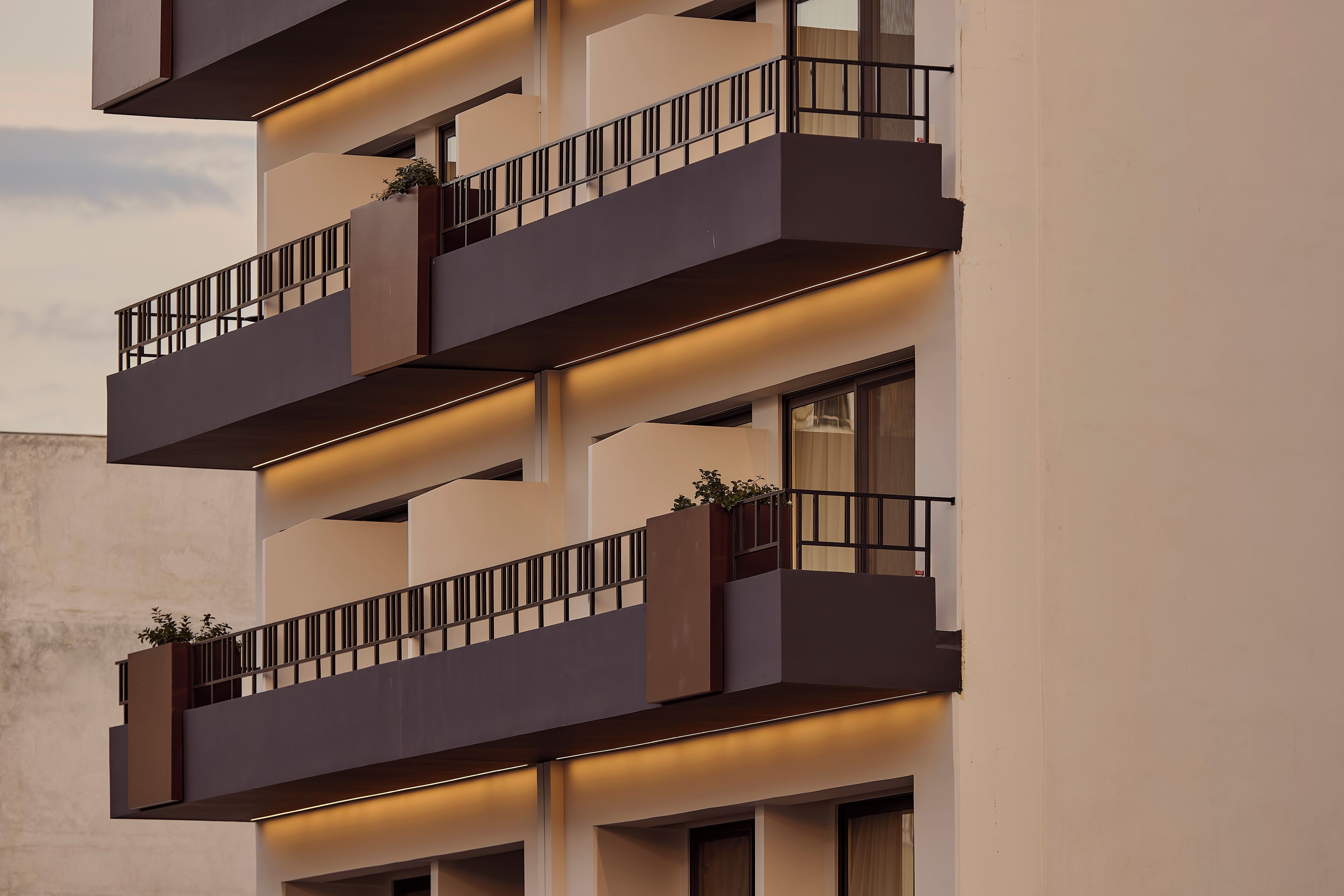 A multi-story building with balconies, railings, and illuminated sections.