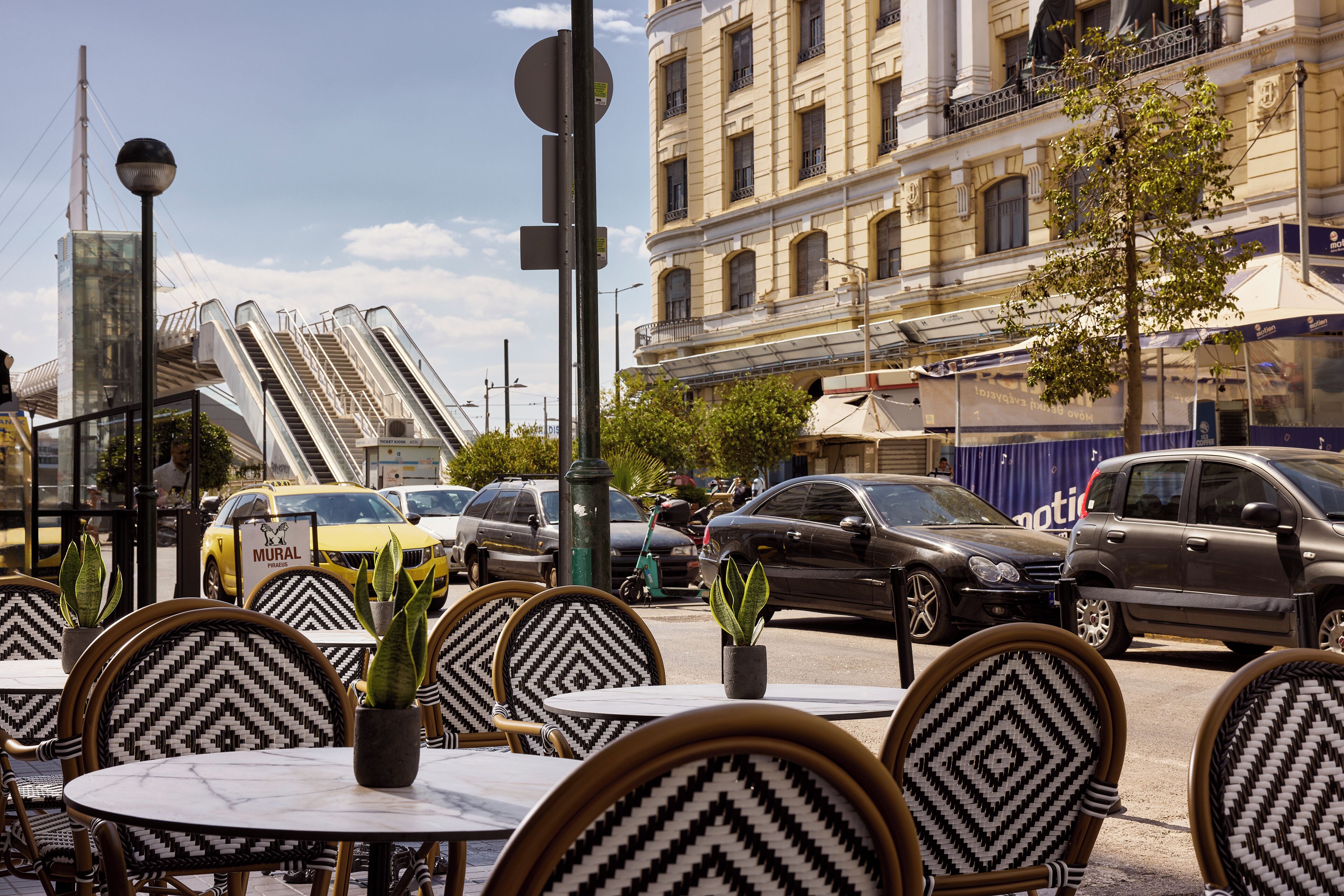 Outdoor seating with patterned chairs, a street with cars, and a building with classical architecture.