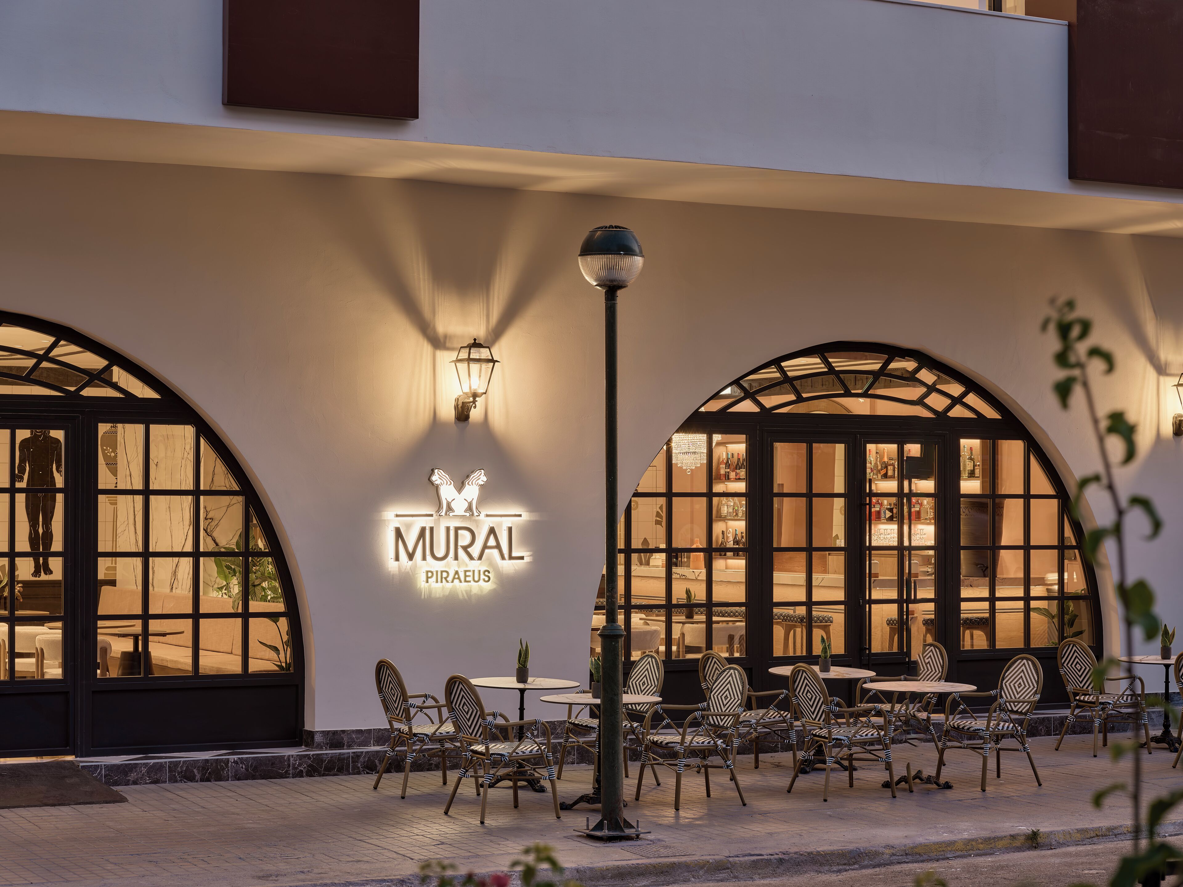 A restaurant with outdoor seating, a sign reading 'MURAL PIRAEUS,' and a decorative lamp post.