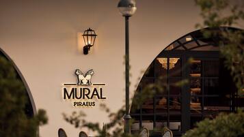 Un restaurant amb un cartell que diu 'MURAL PIRAeus', terrassa amb seients i un fanal.