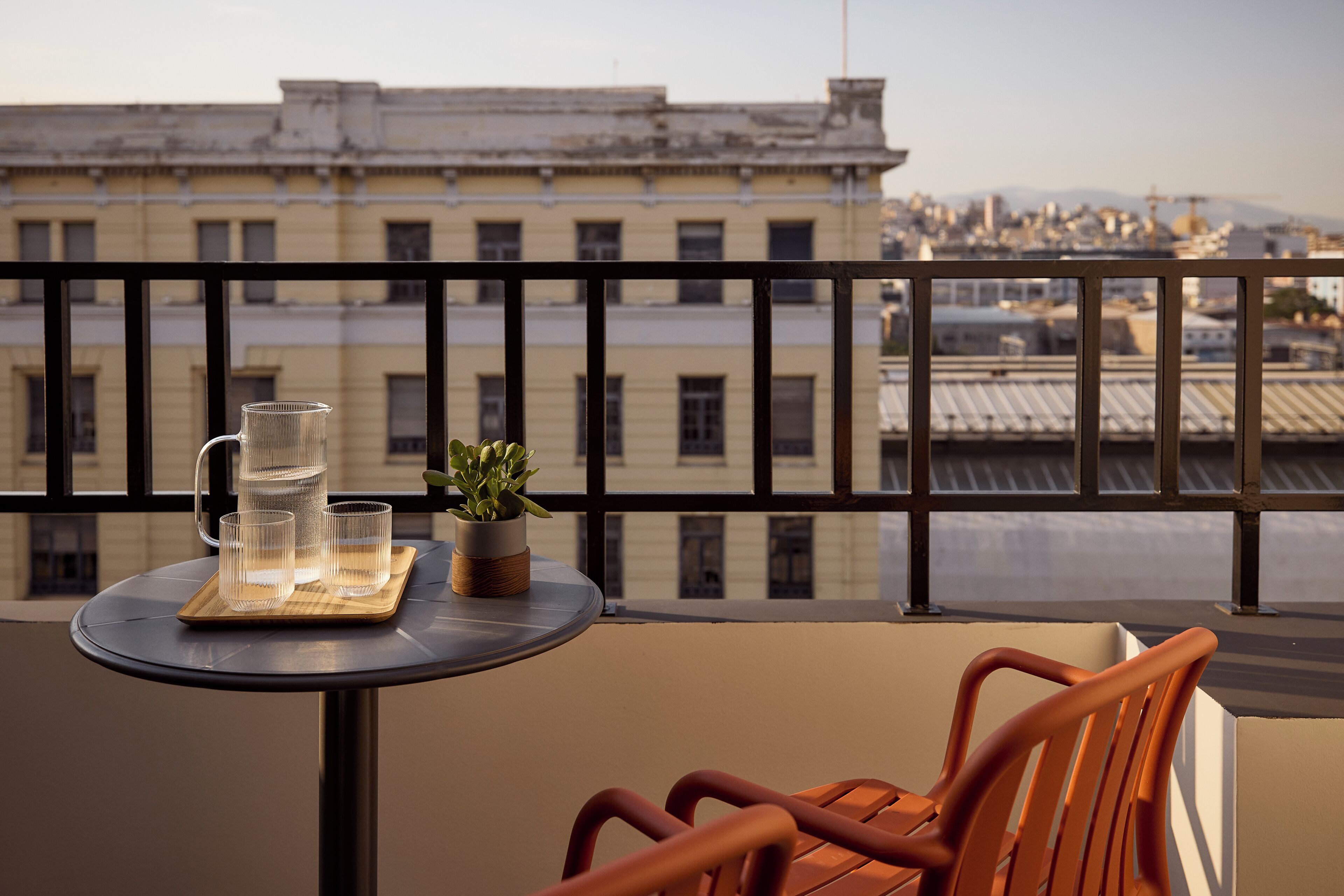 Un balcón con una mesa, una silla, una planta en maceta y una jarrón con agua.