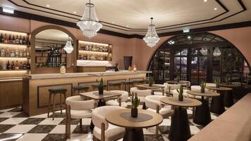 Zona de bar con suelo de cuadros, diferentes distribuciones de asientos y barra con una variedad de botellas.