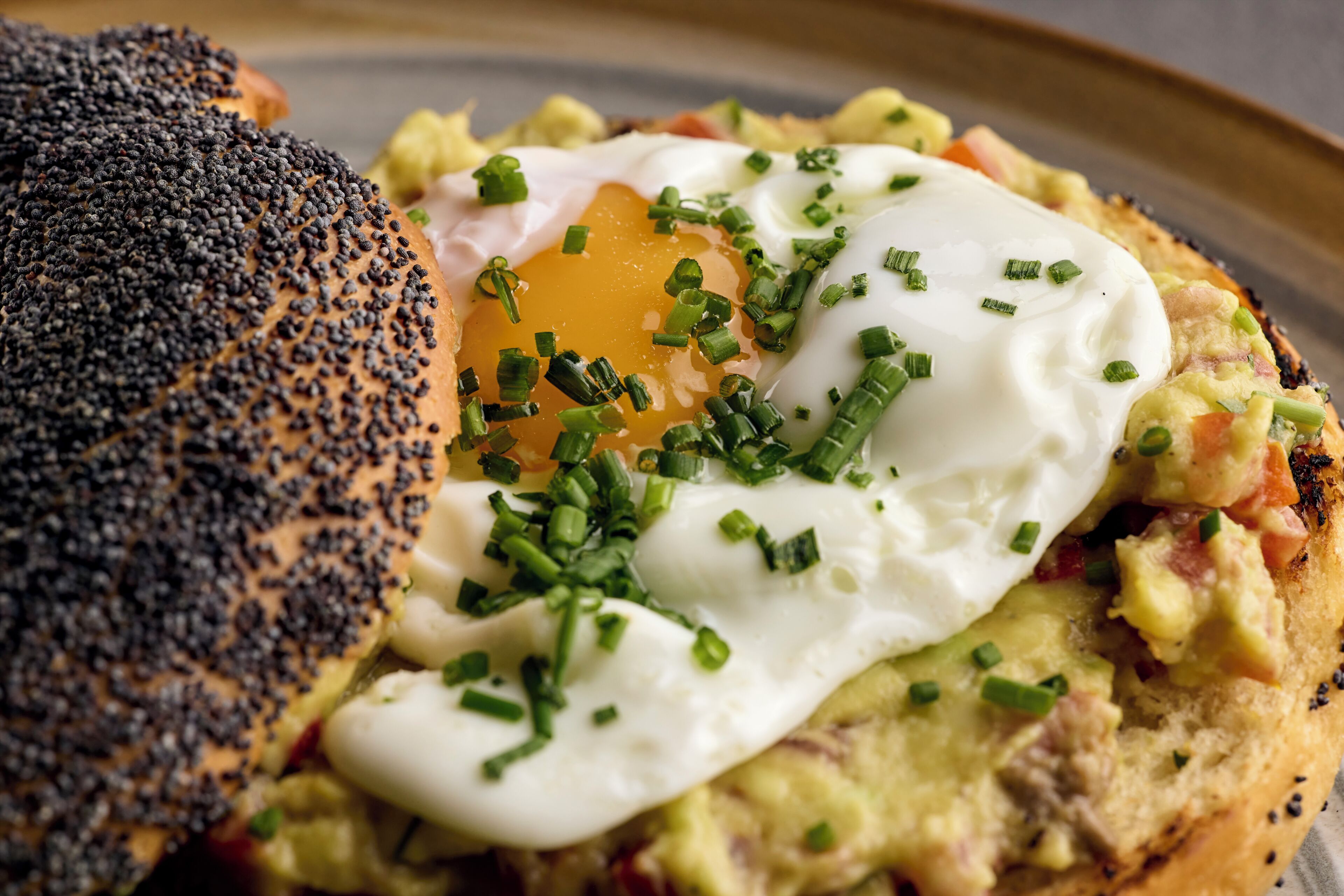 Un plato de desayuno con un huevo pochado, aguacate y cebollín sobre un panecillo de semillas de amapola.