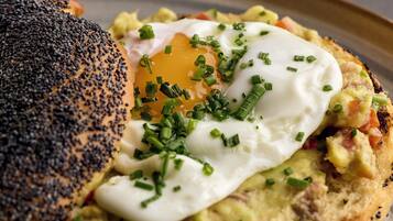 Un plato de desayuno con un huevo pochado, aguacate y cebollín sobre un panecillo de semillas de amapola.