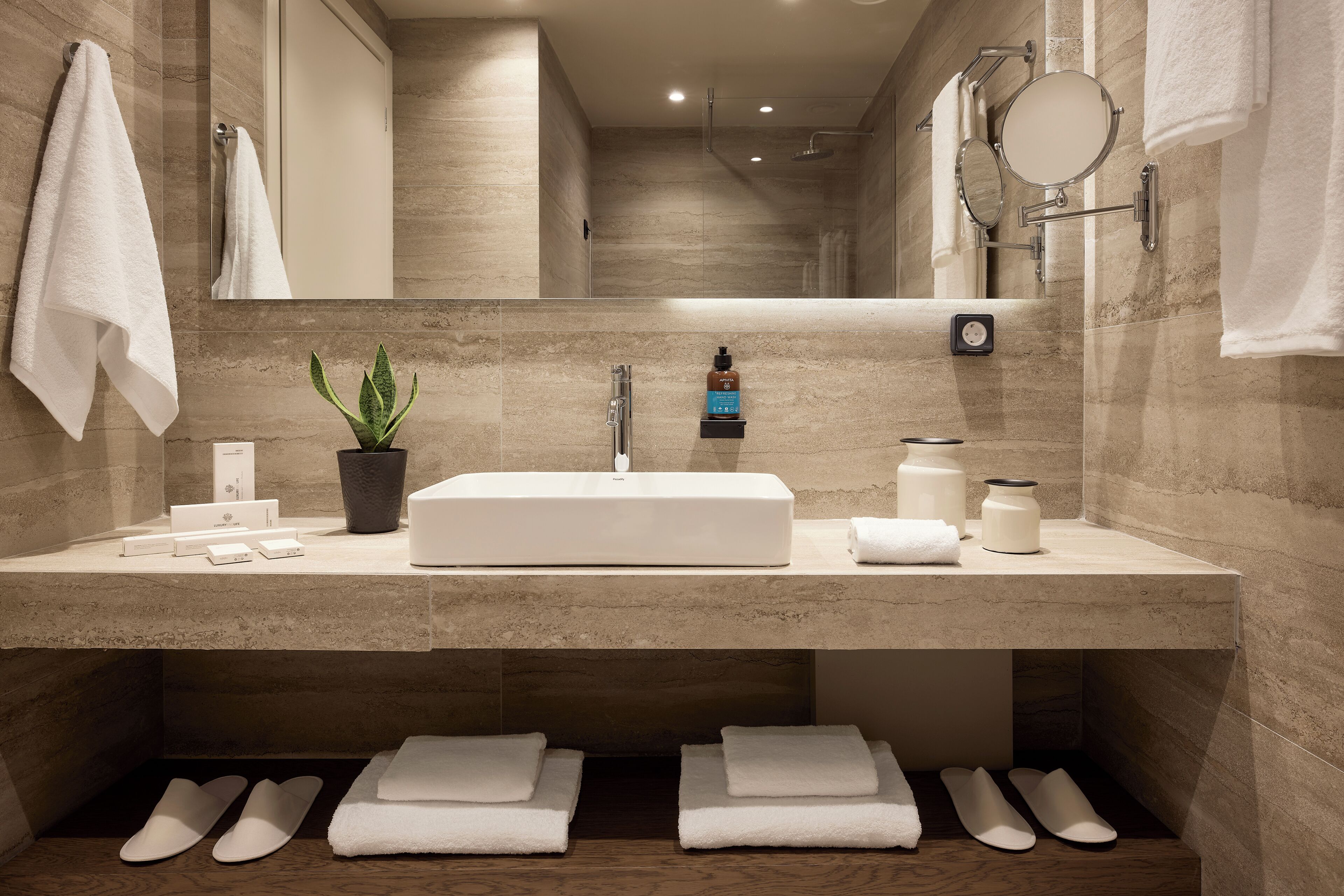 A modern bathroom with a large sink, a mirror, a potted plant, and neatly folded towels.