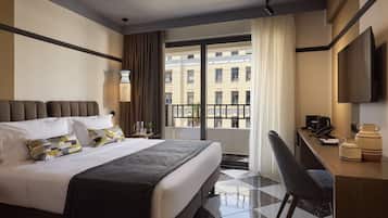 Habitación de hotel con cama, escritorio, silla, televisor y vista al exterior.