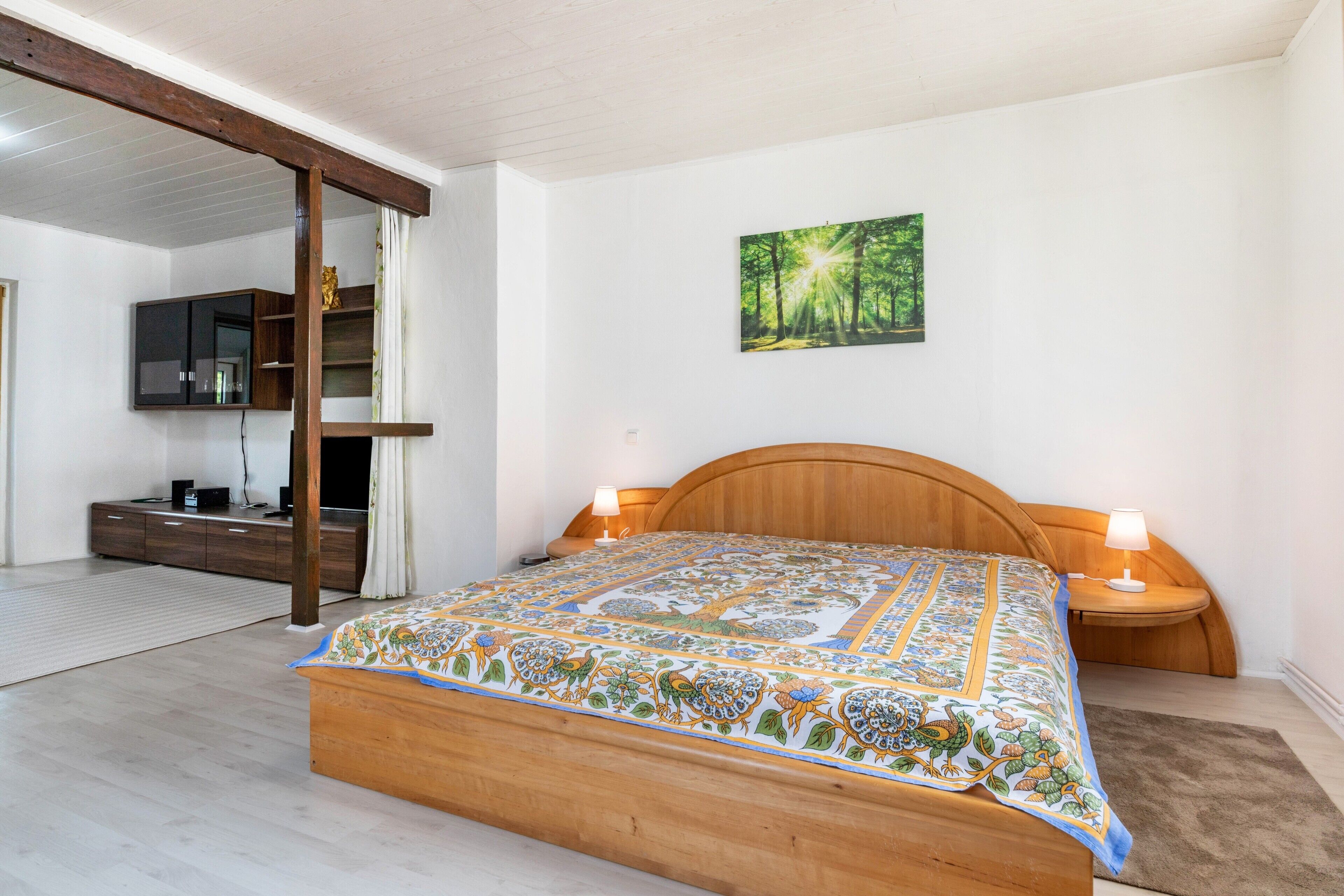 Ein Schlafzimmer mit einem hölzernen Bett, einem Wand-Fernseher, einem Waldbild und einem Holzschrank.