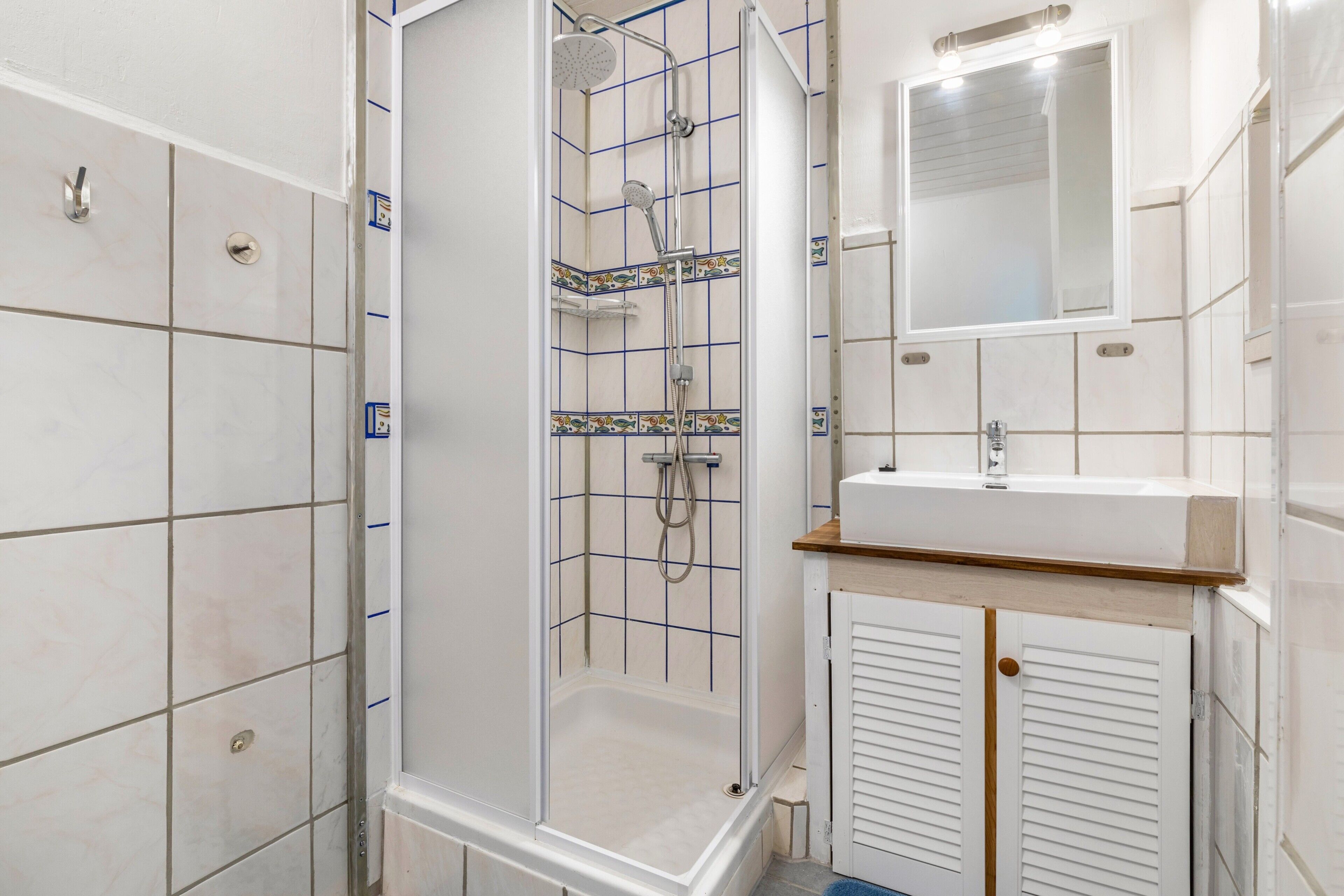 A bathroom with a shower enclosure, a sink, and a mirror.
