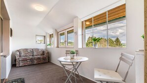 A room with a white sofa, a small round table with a chair, and large windows with wooden blinds.