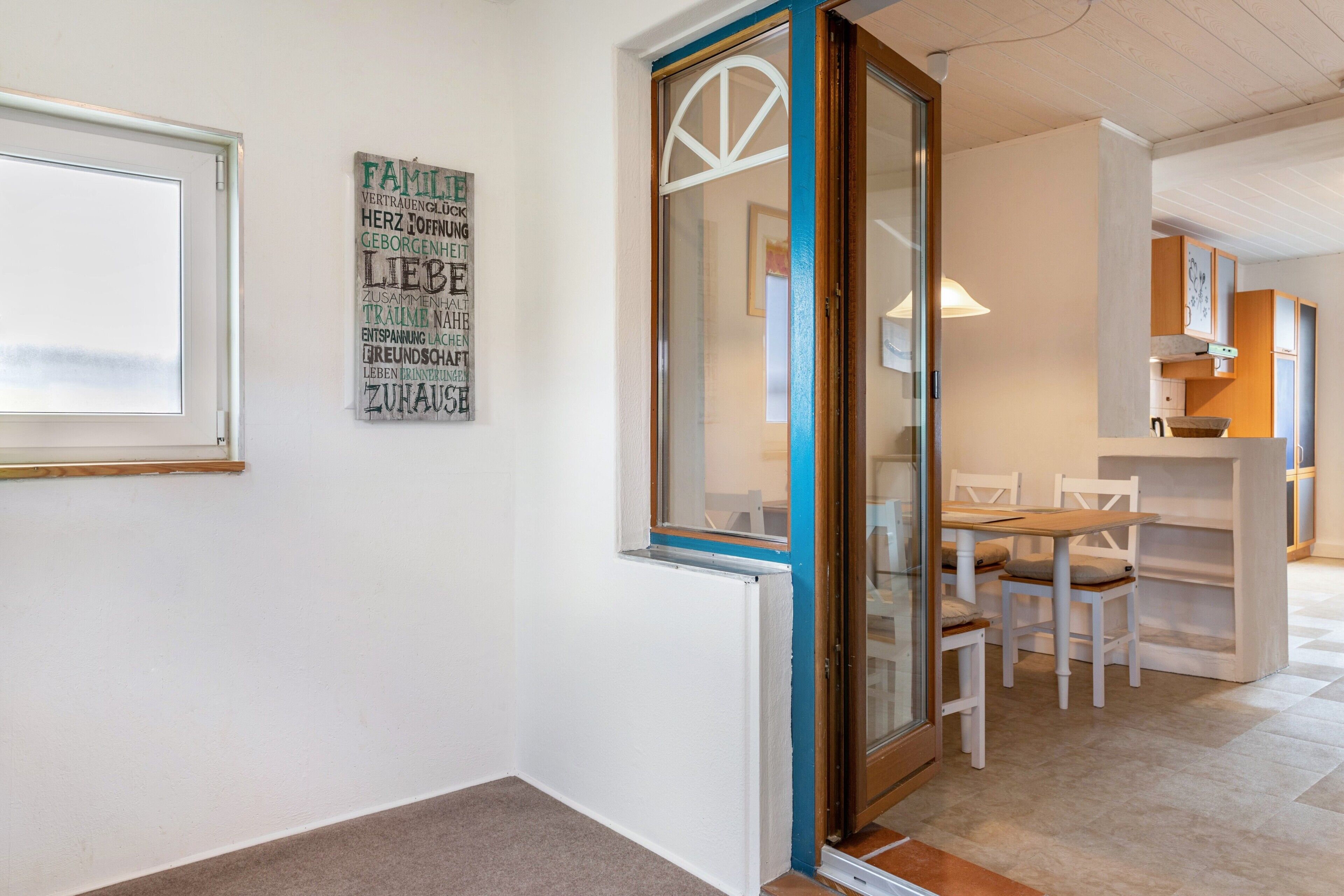 Una habitación con puerta corrediza de vidrio, zona de comedor con mesa y sillas, y cocina con armarios y encimera.