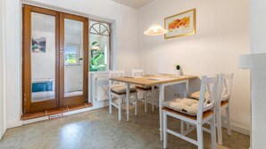 A dining area with a wooden table and white chairs, a pendant light, and a framed picture on the wall.