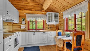 Una cocina estilo cabaña con paredes de madera, gabinetes blancos, una mesa de comedor de madera y un tapete azul.