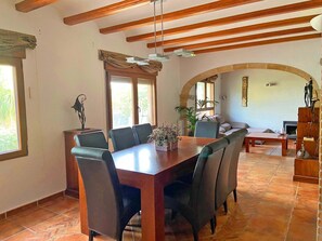 Un espace repas avec une table et des chaises en bois, un plafond avec des poutres apparentes et un sol carrelé.