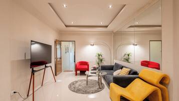 A modern living room with a flat-screen TV, a glass coffee table, a sofa, a yellow armchair, and a red chair.