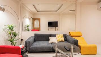 A modern living room with a grey sofa, a yellow armchair, a glass coffee table, and a red chair.