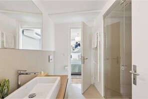 A modern bathroom with a large bathtub, a shower, and a glass door leading to a bedroom. - IKON Old Town Penthouse | AC, Lake & Mountain View (Zürich)