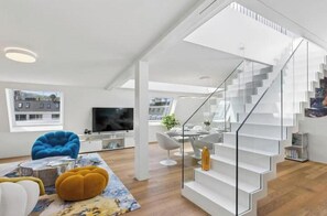 A modern living room with a staircase, a flat-screen TV, and a dining area. - IKON Old Town Penthouse | AC, Lake & Mountain View (Zürich)