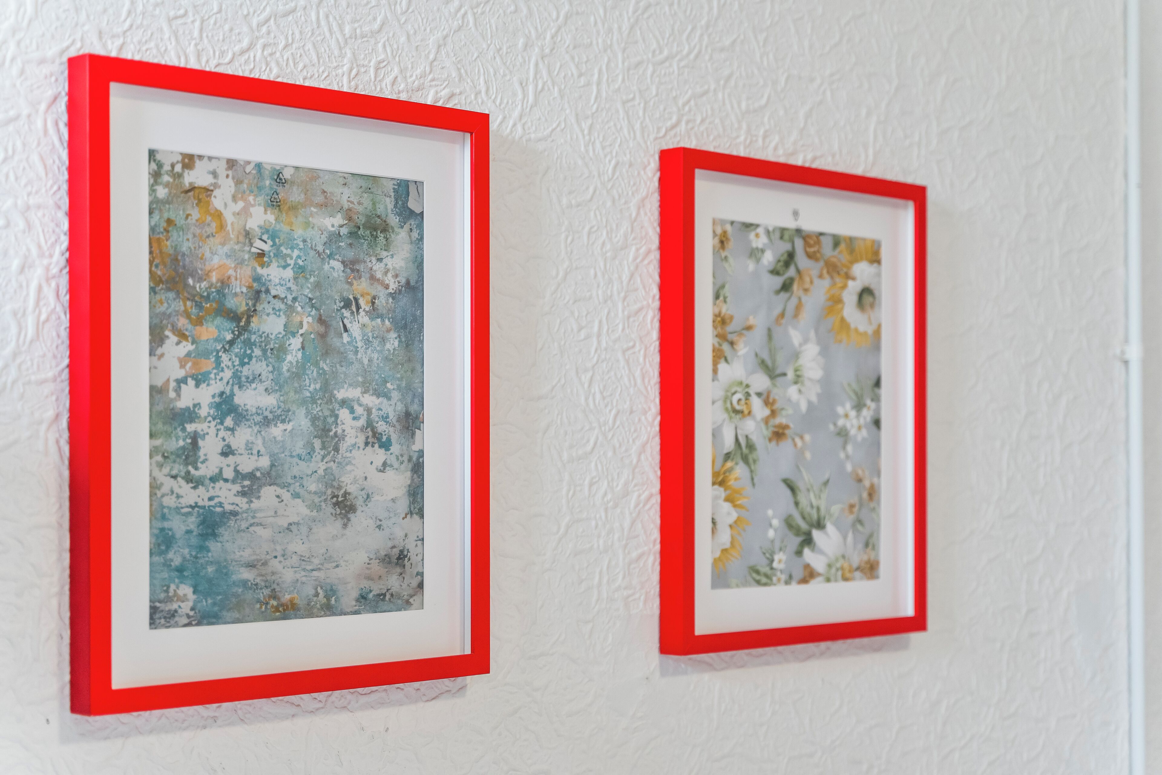 Two framed artworks on a textured white wall.