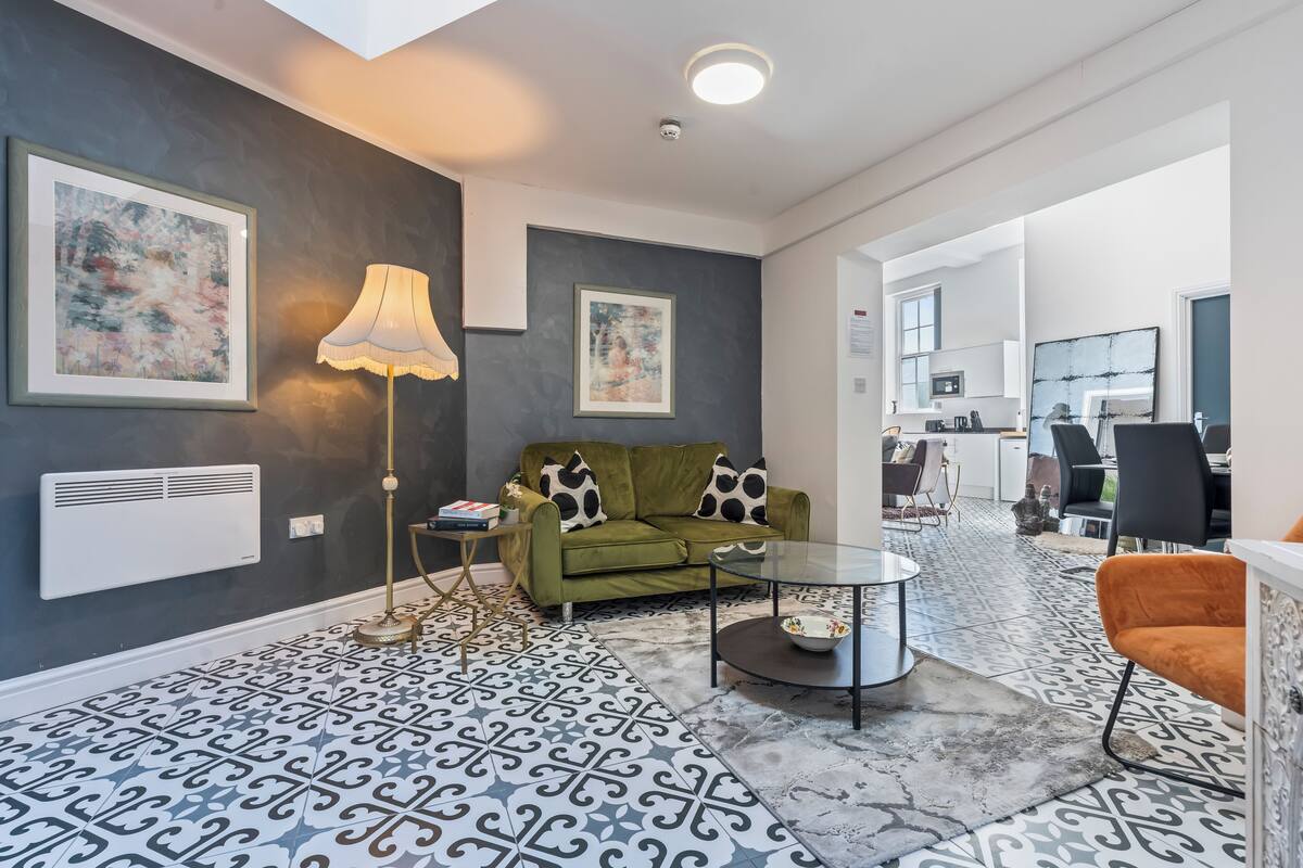 A modern living room with a patterned floor, a green sofa with black and white pillows, a floor lamp, and a glass coffee table.