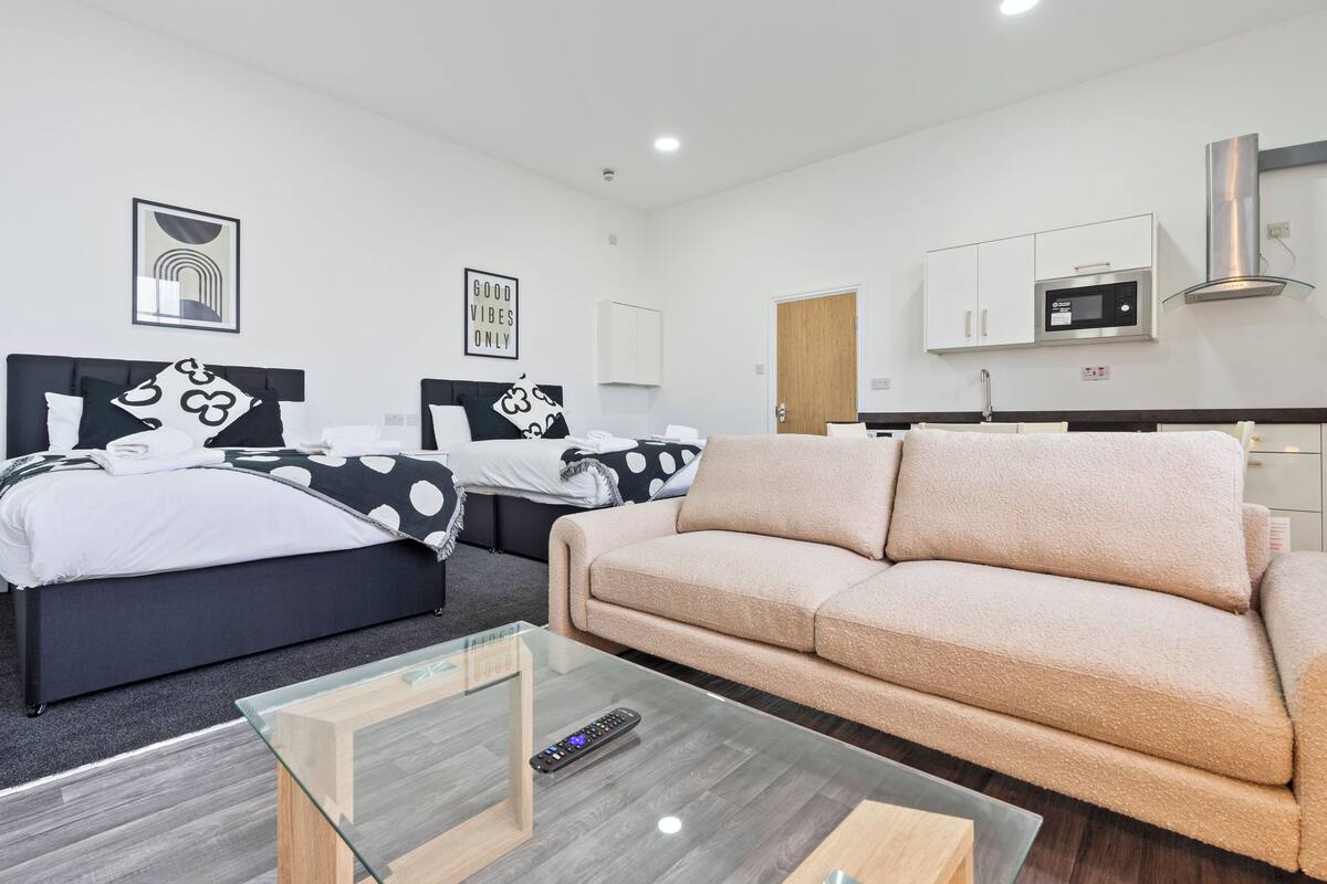 A modern hotel room with two beds, a sofa, a glass coffee table, a microwave, and a cabinet.