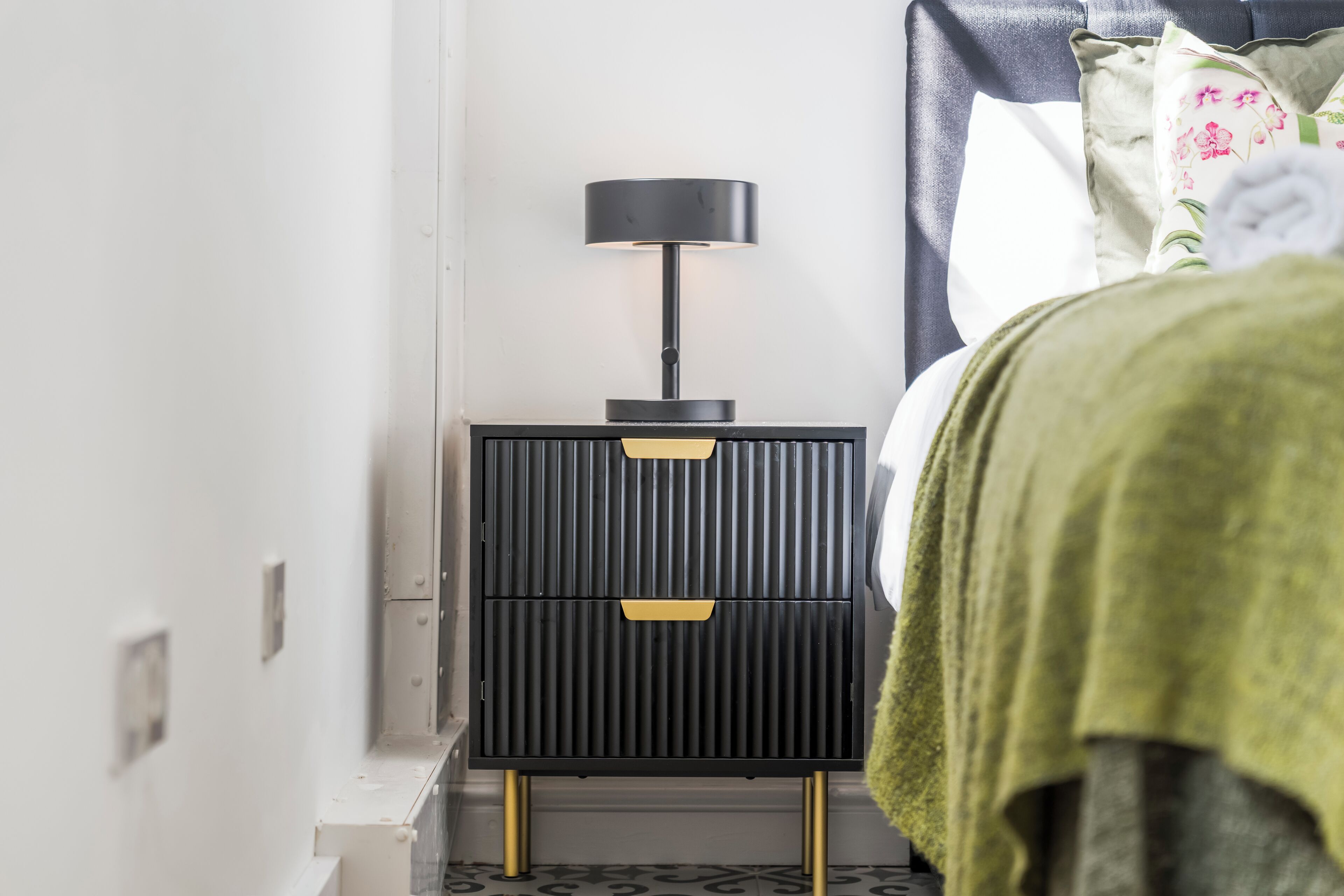 A bedroom with a bed, a bedside table with a lamp, and a green towel.
