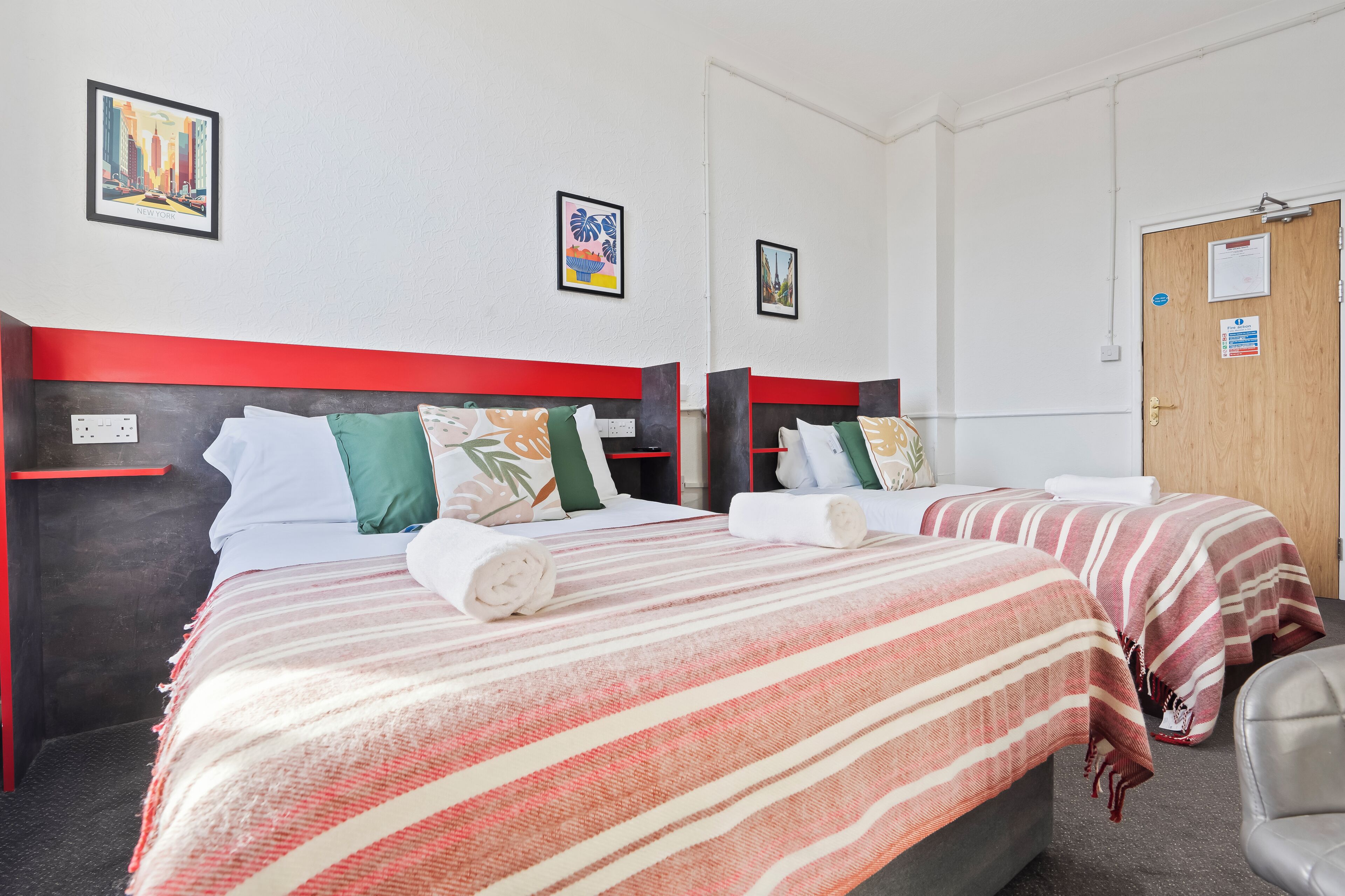 A hotel room with two beds, red and white striped bedding, green and white pillows, and framed artwork on the walls.